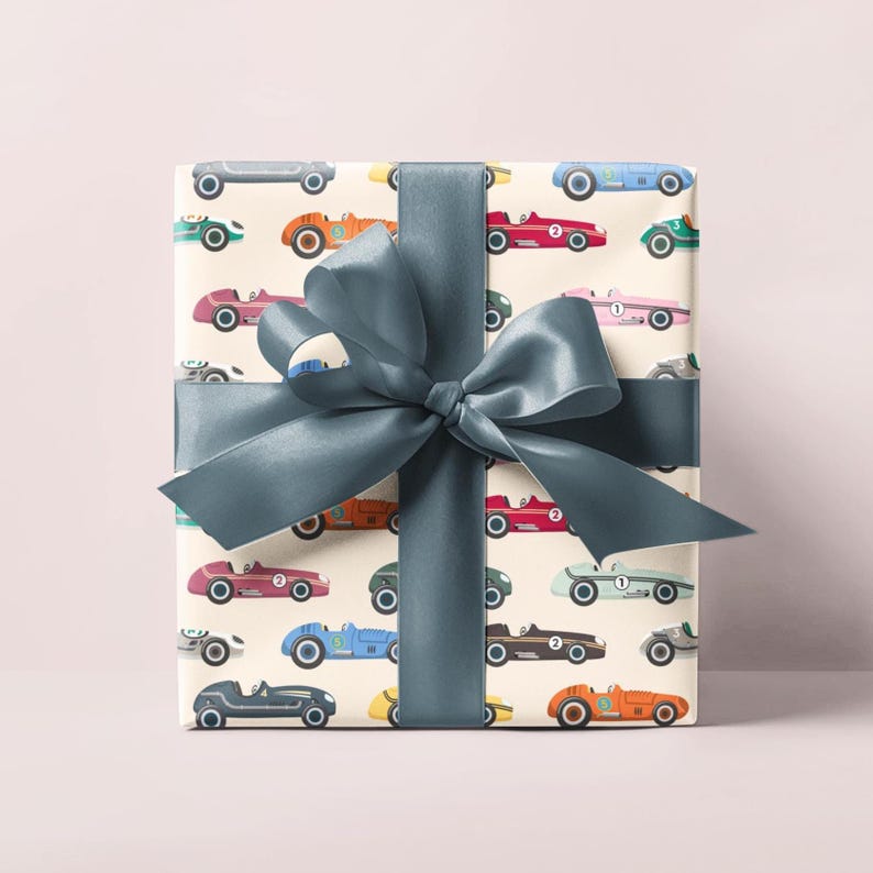 May include: A wrapped gift with cream-colored paper featuring a pattern of colorful vintage race cars. The gift is tied with a wide, teal satin ribbon and bow. The cars are in various colors, including red, blue, orange, and green.