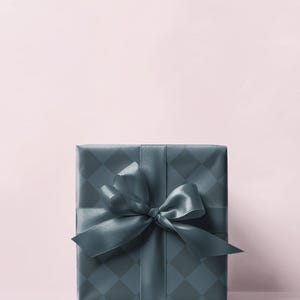 May include: A square gift box wrapped in teal paper with a diamond pattern. A matching teal satin ribbon is tied in a large bow on top. The background is a soft pink.