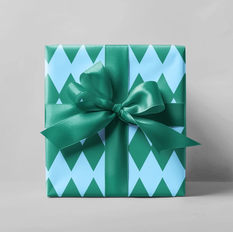 May include: A wrapped gift box with a teal green satin ribbon and bow. The wrapping paper has a light blue and teal green diamond pattern. The gift is presented on a light gray background.