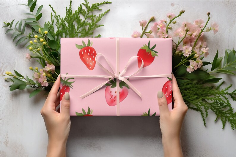 May include: A pink gift box with a white ribbon and a strawberry pattern. The box is wrapped in pink paper with a white ribbon tied in a bow. The paper has a pattern of strawberries on it.