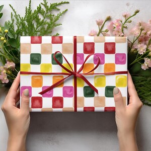 May include: A gift wrapped in white paper with a colorful checkered pattern. The paper has squares of red, pink, orange, yellow, green, and brown. The gift is tied with a red ribbon.