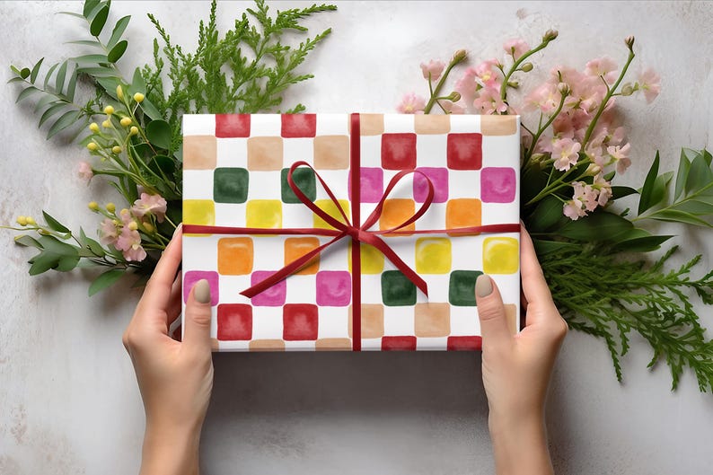 May include: A gift wrapped in white paper with a colorful checkered pattern. The paper has squares of red, pink, orange, yellow, green, and brown. The gift is tied with a red ribbon.