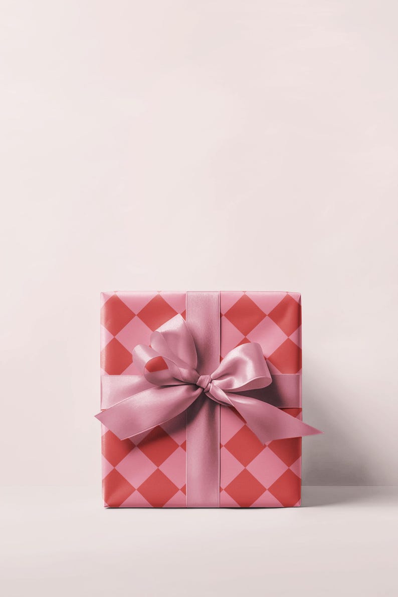 May include: A wrapped gift box with a pink and red diamond pattern. The box is tied with a wide pink satin ribbon and a large bow. The background is a solid light pink.