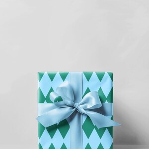 May include: A square gift box wrapped in blue and green diamond patterned paper. A light blue satin ribbon is tied around the box and into a bow. The background is a plain white.