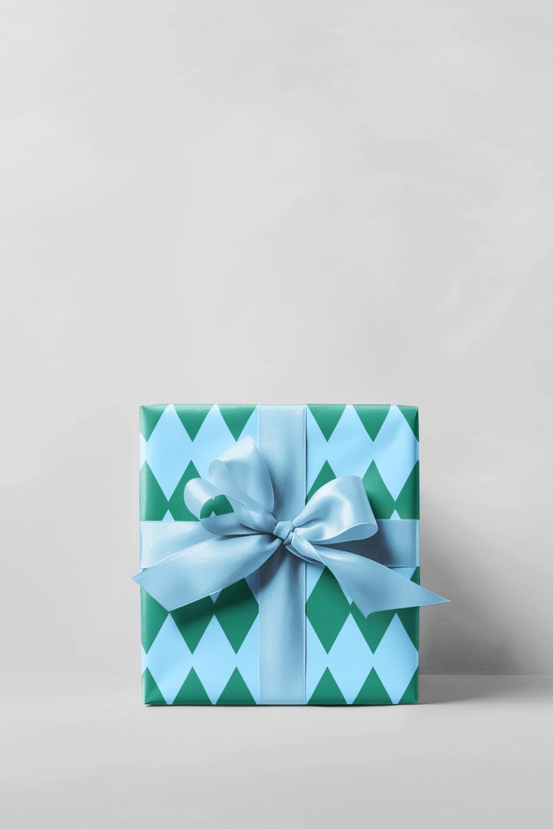 May include: A square gift box wrapped in blue and green diamond patterned paper. A light blue satin ribbon is tied around the box and into a bow. The background is a plain white.