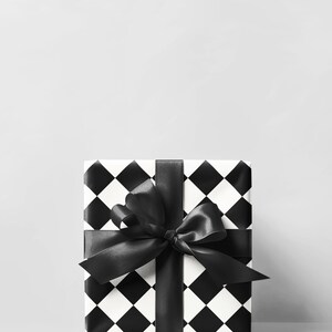May include: A wrapped gift box with a black and white checkered pattern. The box is tied with a wide black satin ribbon and bow. The background is a solid light gray.