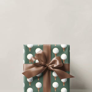 K&ouml;nnte beinhalten: Ein verpacktes Geschenk mit dunkelgr&uuml;nem Papier, das mit wei&szlig;en Golfb&auml;llen auf Abschl&auml;gen gemustert ist. Ein braunes Satinband ist als Schleife um das Paket gebunden. Der Hintergrund ist einfarbig hellbeige.