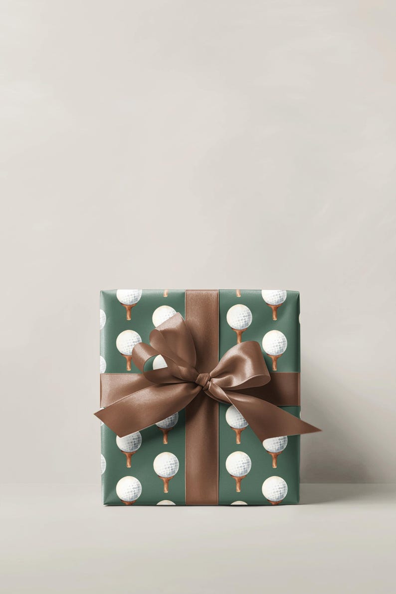 K&ouml;nnte beinhalten: Ein verpacktes Geschenk mit dunkelgr&uuml;nem Papier, das mit wei&szlig;en Golfb&auml;llen auf Abschl&auml;gen gemustert ist. Ein braunes Satinband ist als Schleife um das Paket gebunden. Der Hintergrund ist einfarbig hellbeige.