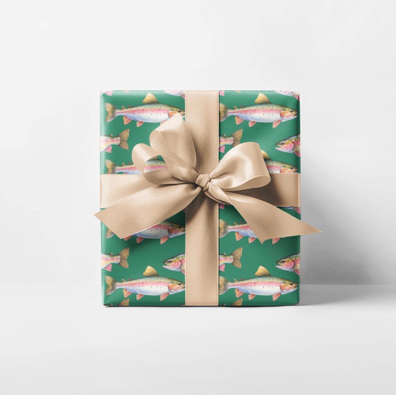 May include: A wrapped gift box featuring a green background with a repeating pattern of watercolor rainbow trout. The box is tied with a tan satin ribbon and bow. The gift wrap is suitable for fishing enthusiasts.