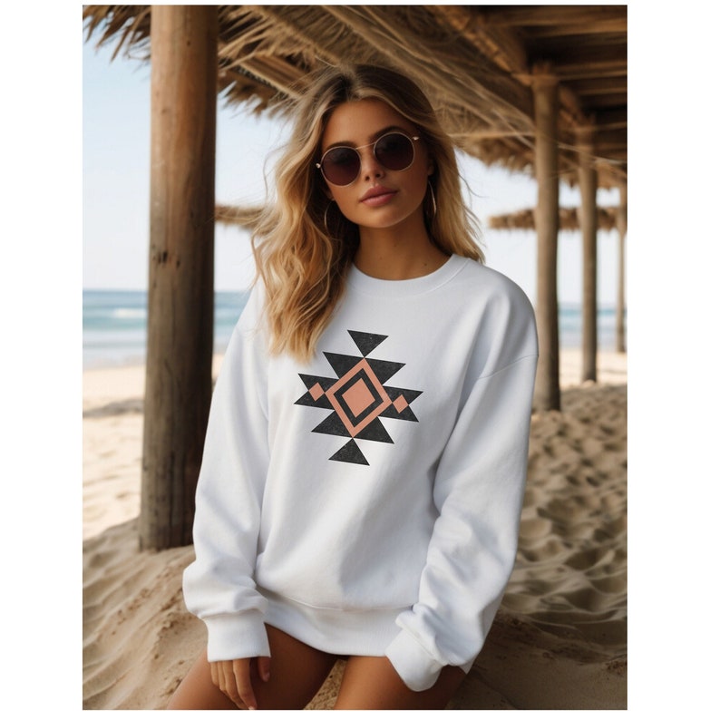 May include: White sweatshirt featuring a geometric design in black, peach, and white. The design incorporates a diamond shape at the centre surrounded by triangles.