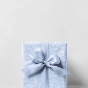 Puede incluir: Una caja de regalo azul claro con un patr&oacute;n floral blanco y una cinta de sat&eacute;n azul claro a juego atada en un lazo.