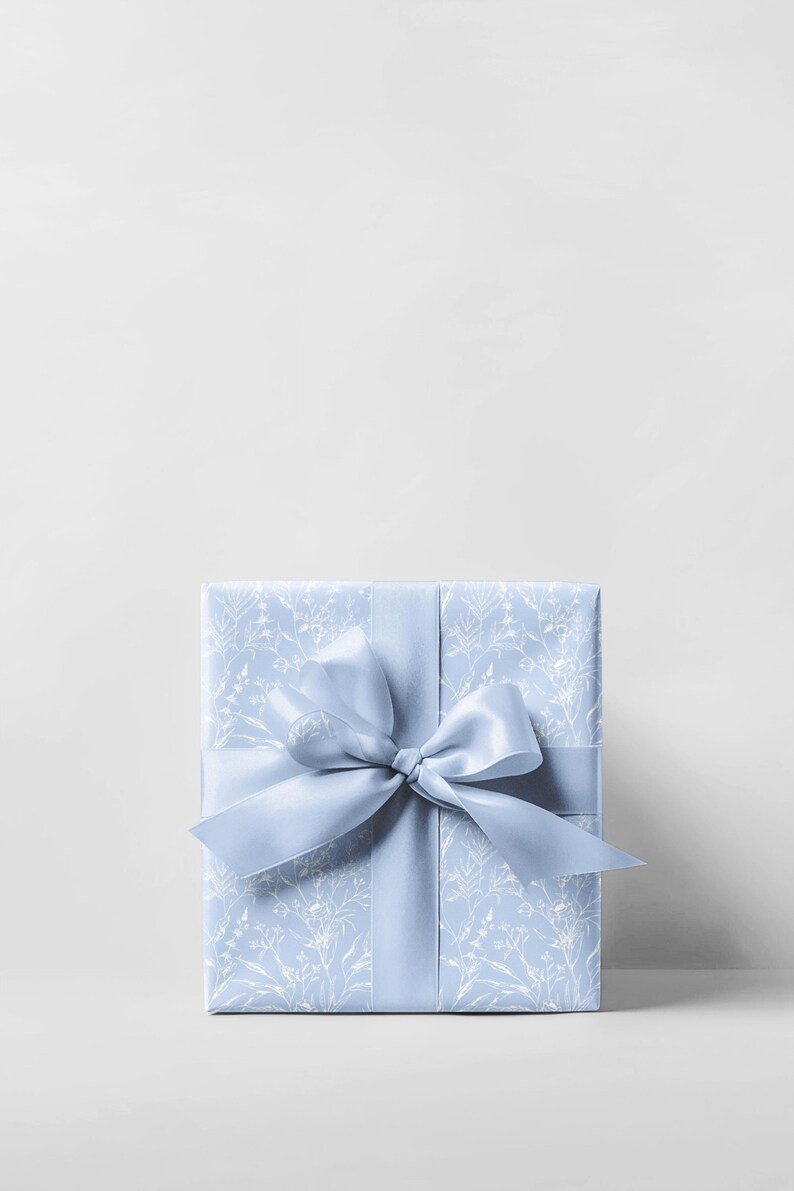 Puede incluir: Una caja de regalo azul claro con un patr&oacute;n floral blanco y una cinta de sat&eacute;n azul claro a juego atada en un lazo.