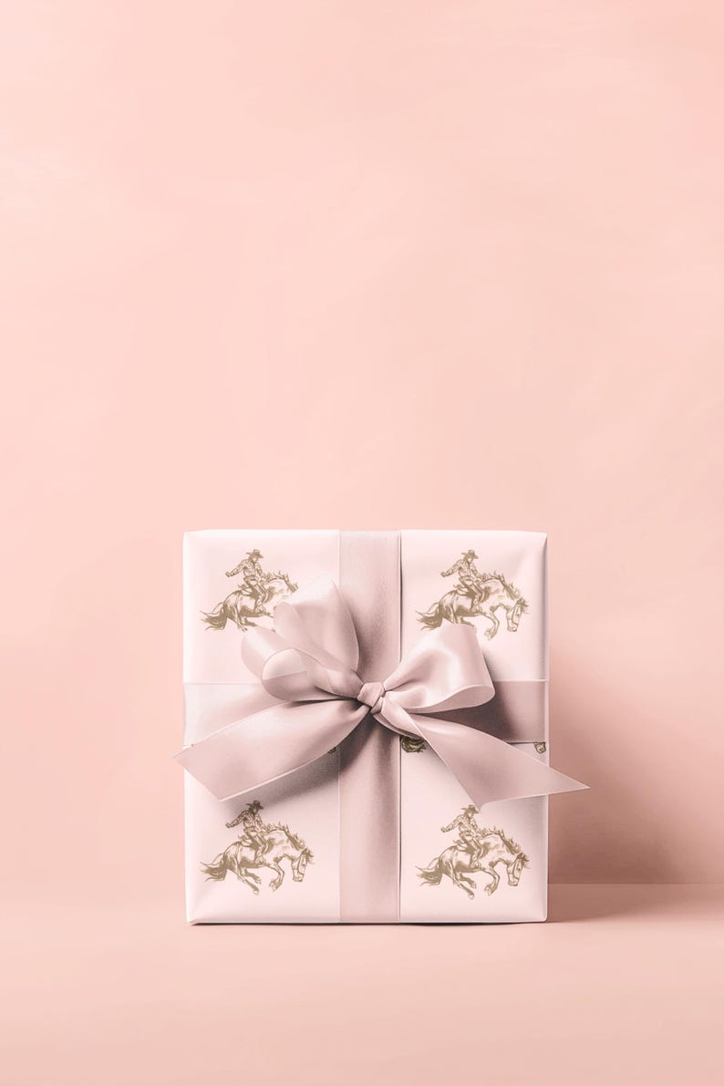 May include: A wrapped gift box with a light pink background. The gift wrap is white with a repeating gold illustration of a cowboy riding a horse. A light pink ribbon and bow are tied around the box.