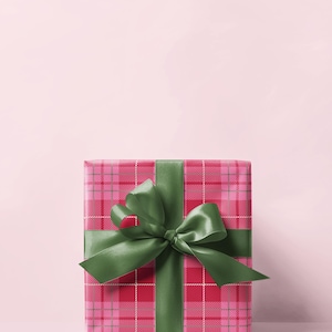 May include: A square gift box wrapped in red and pink plaid paper, tied with a large green satin bow. The bow is centered on the box, and the ribbon wraps around the box. The background is a solid light pink.