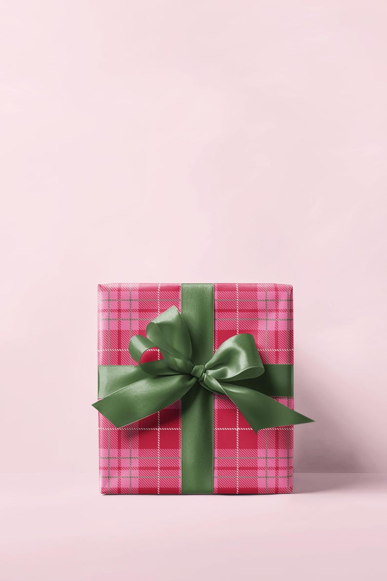 May include: A square gift box wrapped in red and pink plaid paper, tied with a large green satin bow. The bow is centered on the box, and the ribbon wraps around the box. The background is a solid light pink.