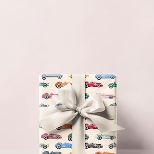 May include: A wrapped gift with a cream-colored paper featuring a pattern of vintage race cars in various colors. The gift is tied with a large, light gray satin bow.