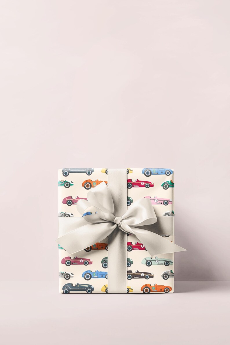 May include: A wrapped gift with a cream-colored paper featuring a pattern of vintage race cars in various colors. The gift is tied with a large, light gray satin bow.