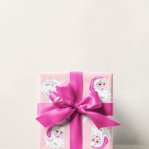 Puede incluir: Un regalo envuelto con papel rosa con caras de Pap&aacute; Noel. El regalo est&aacute; atado con una cinta y un lazo de sat&eacute;n rosa brillante. El tema es la Navidad y la entrega de regalos.