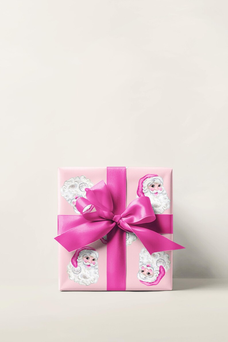 Puede incluir: Un regalo envuelto con papel rosa con caras de Pap&aacute; Noel. El regalo est&aacute; atado con una cinta y un lazo de sat&eacute;n rosa brillante. El tema es la Navidad y la entrega de regalos.