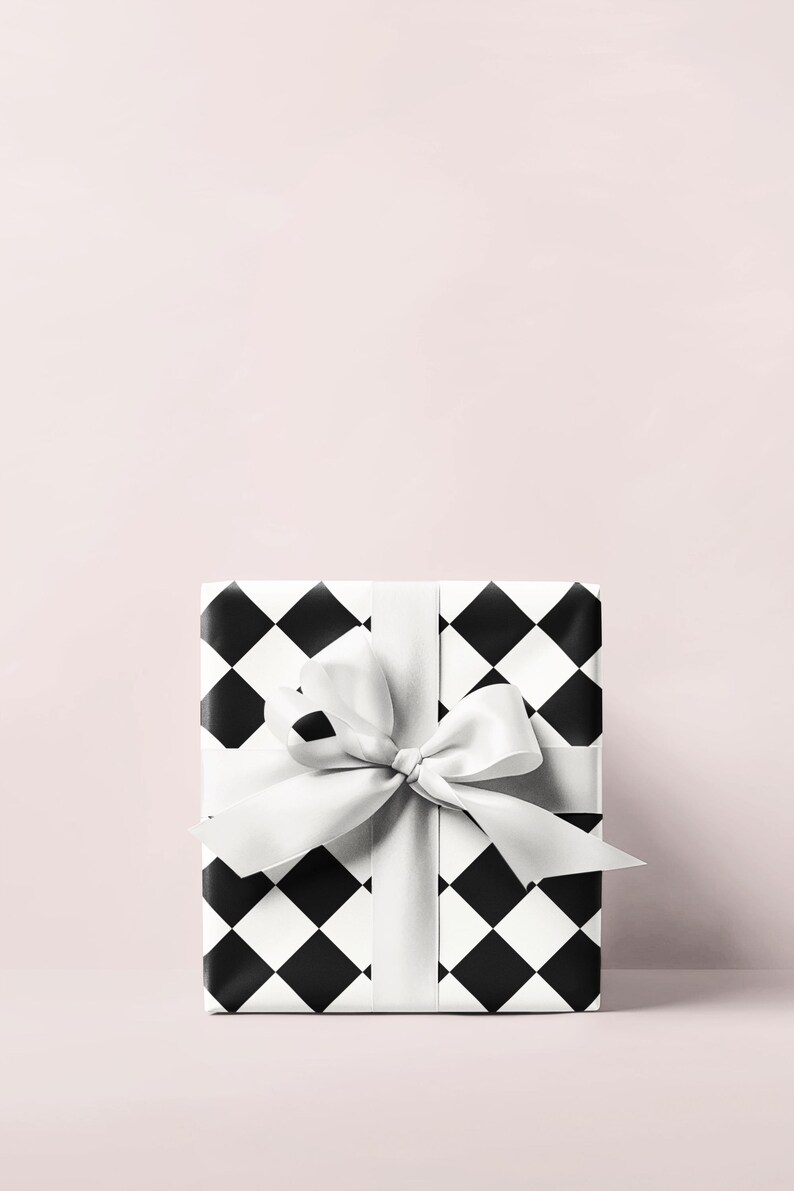 May include: A wrapped gift box with a black and white diamond pattern. The box is tied with a white satin ribbon and bow. The background is a solid light pink.