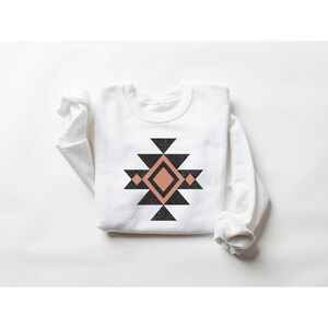 May include: White long-sleeved sweatshirt with a black and peach geometric design on the front. The design is a stylised Native American pattern.