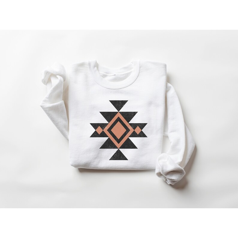 May include: White long-sleeved sweatshirt with a black and peach geometric design on the front. The design is a stylised Native American pattern.