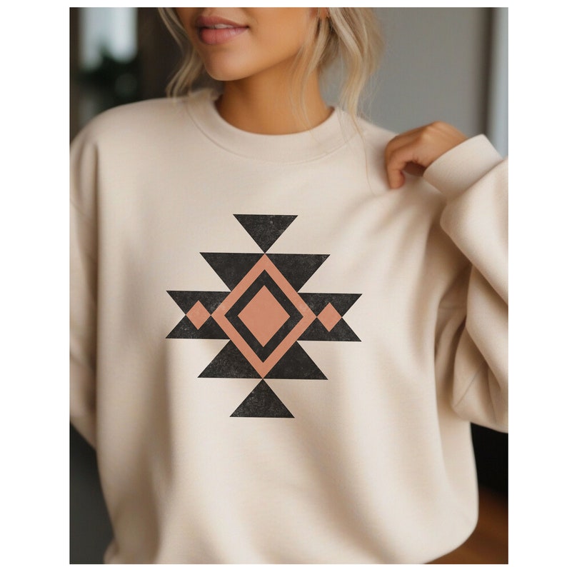 May include: A cream-coloured sweatshirt with a black and peach geometric design. The design features a large diamond shape with smaller diamonds and triangles surrounding it.