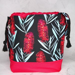 May include: A black drawstring bag with a red trim and a floral print featuring red and blue flowers. The bag has a black drawstring and a black tassel.