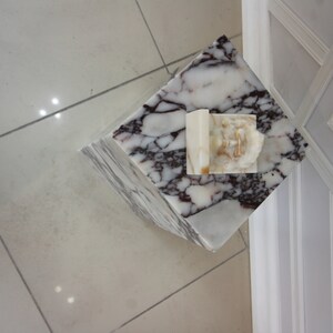May include: A white marble pedestal with a white and brown marble top. The pedestal has a white marble sculpture on top.
