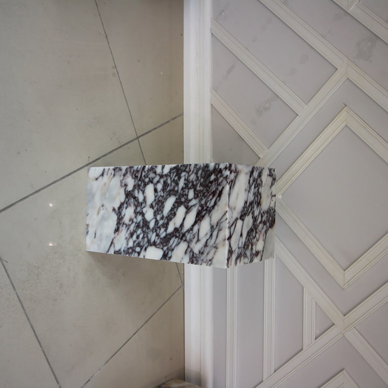 May include: A white marble pedestal with black and gray veining. The pedestal is rectangular and has a smooth, polished surface.