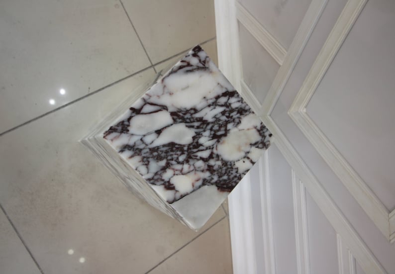 May include: A white marble pedestal with a square top and a swirling pattern of dark red and purple veins.