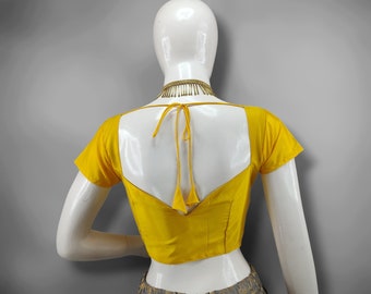 May include: A yellow short-sleeved blouse with a square neckline and a tie closure at the back. The blouse is displayed on a mannequin, paired with a grey and gold patterned skirt. A gold-coloured necklace is visible.