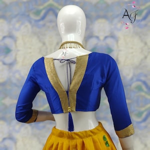 May include: A blue and gold blouse with a V-neck and a tassel tie. The blouse has a gold trim and a blue tassel.