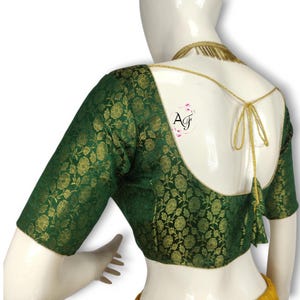 Peut inclure: Un chemisier brodé vert avec un motif floral doré et une bordure dorée. Le chemisier a un dos bas avec une fermeture à nouer et un pompon.