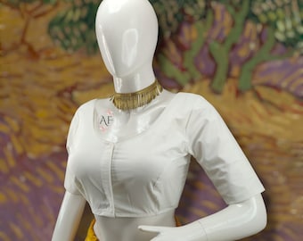 May include: White cotton blouse with a scoop neck and short sleeves. The blouse has a button-up front and a gold fringe choker necklace.
