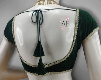 May include: A dark green velvet blouse with short sleeves and a low back. The edges are trimmed with gold-colored lace. The back features a tie closure with two tassels. A gold-colored necklace is visible at the neckline.