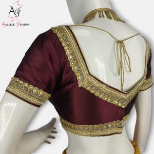 May include: A maroon silk blouse with gold embroidery and embellishments. The blouse has a deep V-neckline and short sleeves.