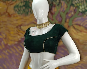 May include: A dark green velvet crop top with gold trim and a scoop neckline. The top is on a white mannequin with a gold necklace.