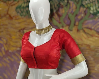 May include: A red silk blouse with gold trim on the sleeves and neckline. The blouse has a button closure at the front and a scoop neckline.