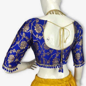 Könnte beinhalten: Eine königsblaue Bluse mit goldenen Blumenmustern und Dreiviertelärmeln. Die Bluse hat einen tiefen Rückenausschnitt mit goldenem Bindeband und ist mit blauen Perlen verziert. Der untere Teil der Bluse ist gelb.