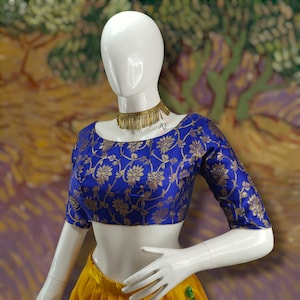 May include: A blue and gold brocade blouse with a floral pattern. The blouse has a square neckline and short sleeves.