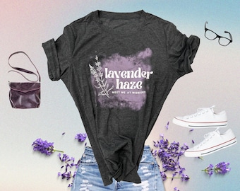 May include: A grey t-shirt with a lavender haze design and the text "lavender haze meet me at midnight". The shirt is paired with blue jeans and white trainers.