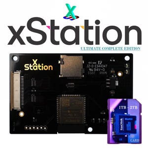 Könnte beinhalten: Schwarze xStation-Leiterplatte mit goldfarbener Schrift und einer kleinen SD-Karte. Der Text "xStation ULTIMATE COMPLETE EDITION" wird über der Platine angezeigt. Eine lila SD-Karte mit "1TB - 2TB" und "SanDisk SD CARD" ist ebenfalls abgebildet.