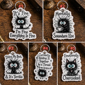 May include: A collection of five white keychains with a cartoon monster design. Each keychain has a different phrase, including "It's Fine, I'm Fine, Everything Is Fine" and "Emotionally Overcooked". The keychains have a silver keyring.