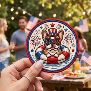 May include: Circular embroidered patch with a French Bulldog wearing patriotic glasses and a hat, floating in a red, white, and blue inner tube. The design includes fireworks and stars, ideal for celebrating Independence Day.