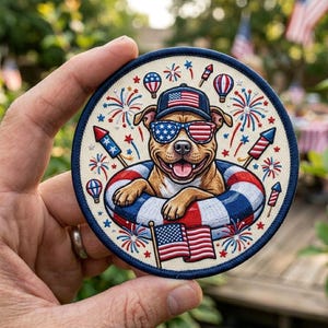 May include: Circular patch with a smiling dog wearing sunglasses and a hat, both decorated with the American flag. The dog is in a red, white, and blue inner tube, surrounded by fireworks and balloons. The patch has a blue border.