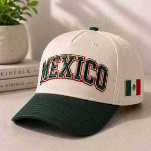 May include: A cream-coloured baseball cap featuring the word MEXICO embroidered in dark green with a red outline across the front panels. The cap has a dark green brim and a small rectangular patch of the Mexican flag on the side panel.