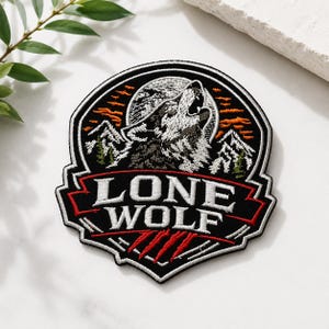 May include: A circular embroidered patch featuring a howling wolf silhouette against a full moon, snowy mountain peaks, and orange clouds. The text LONE WOLF is stitched in white capital letters on a black background with red claw marks below.