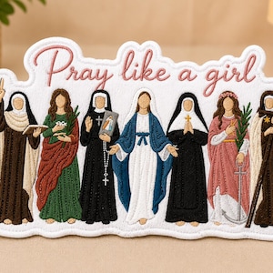May include: Embroidered patch depicting seven figures in religious garments. The pink script text reads "Pray like a girl". The figures are in brown, green, black, and blue. The patch has a white background with a stitched border.
