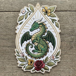 May include: Embroidered patch featuring a green dragon with gold accents, wings, and horns, set against a white background with a gold border. The design is surrounded by floral elements, including roses and leaves, creating a fantasy theme.